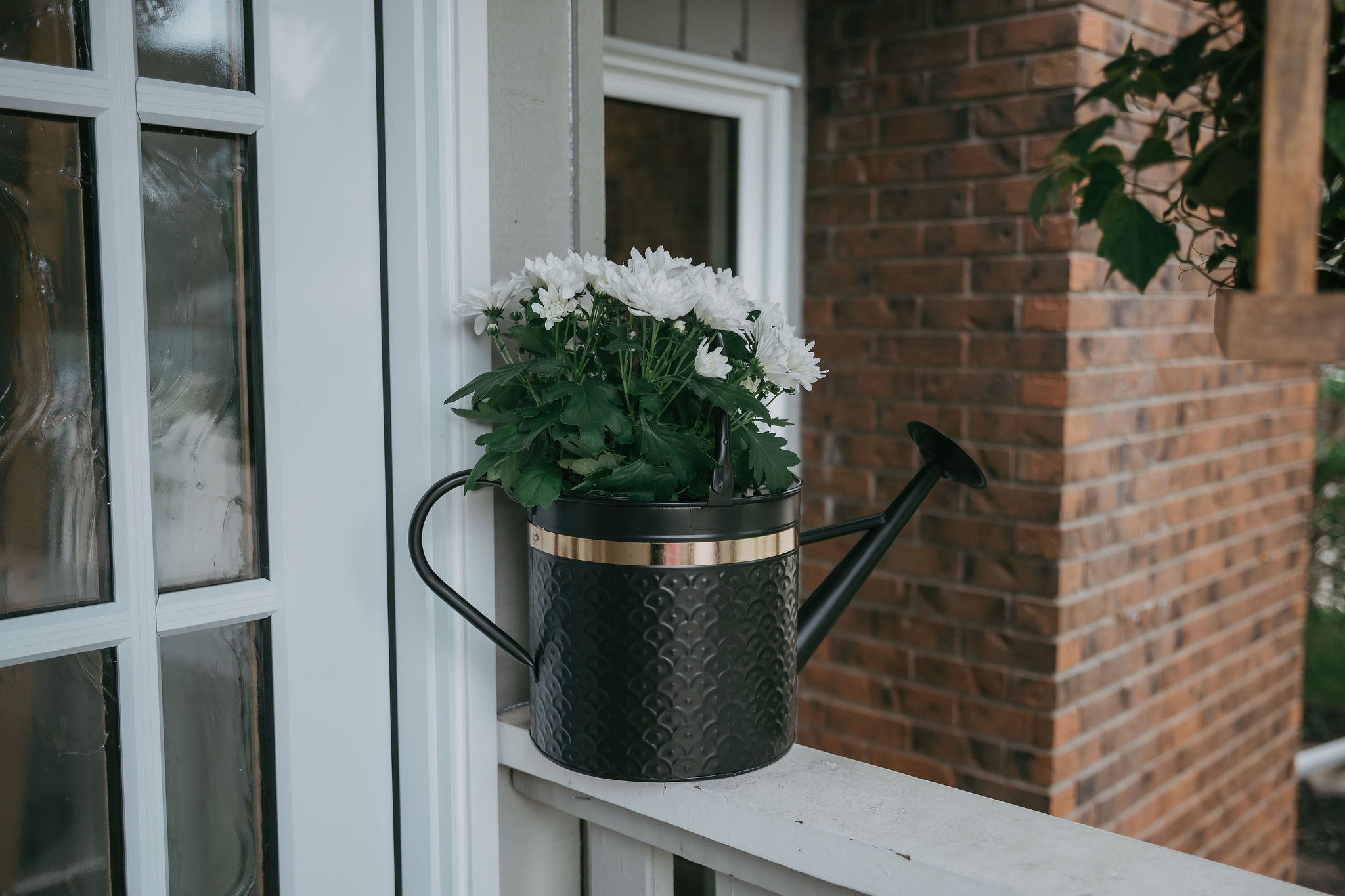 Upcycled black watering can with flowers on front porch